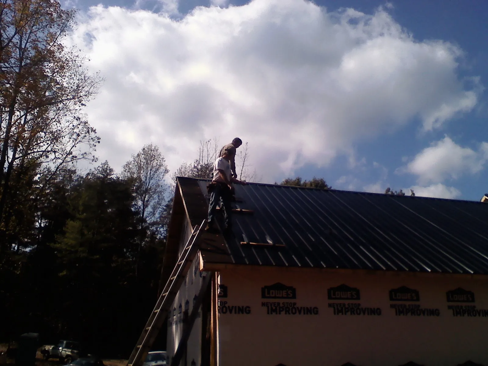 Roofer fastening dark metal panels high against a cloudy sky, from a Roof Inspection job in Augusta